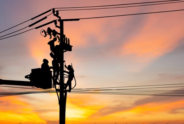 Line workers fix electrical pole during sunset